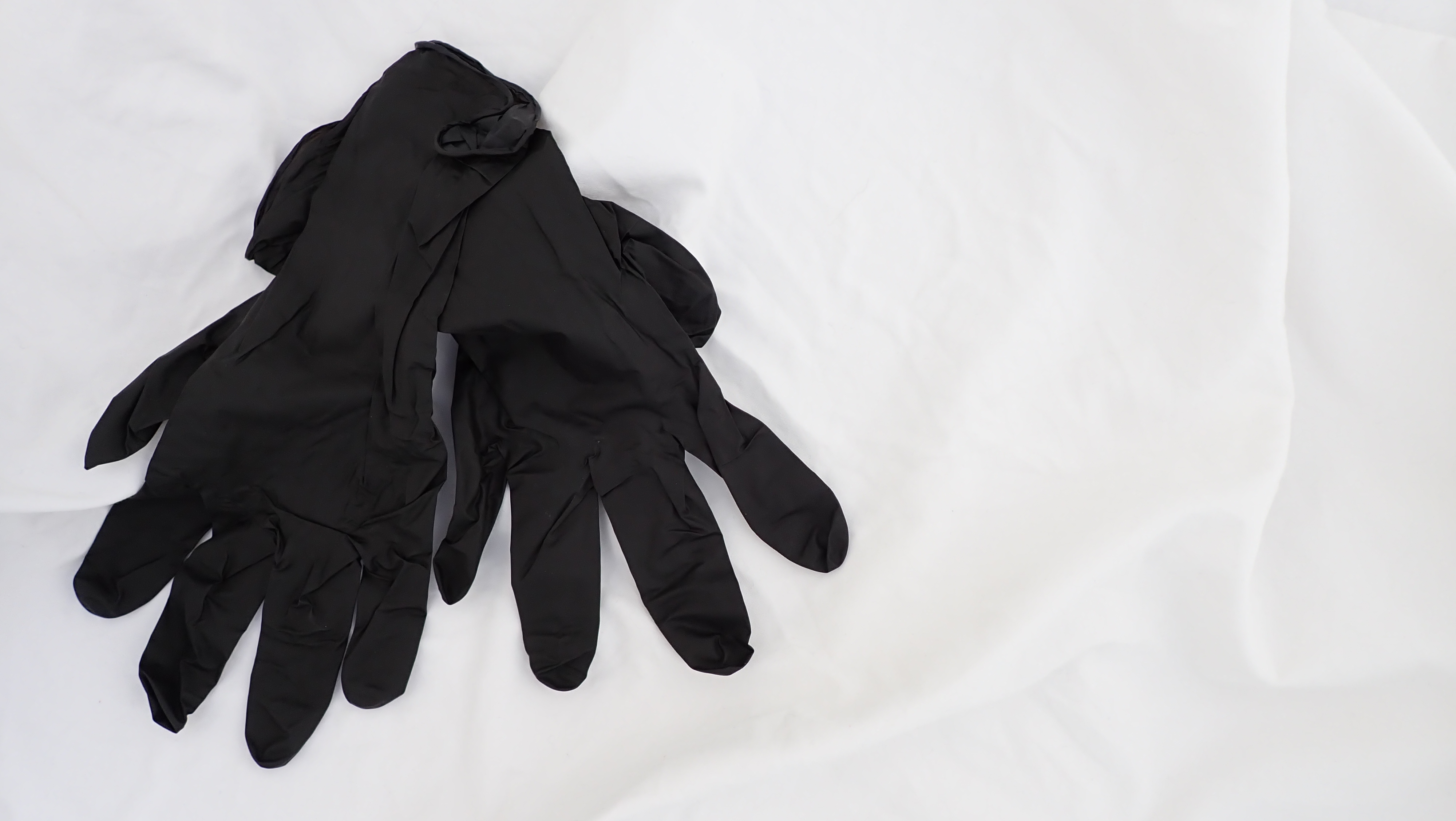 two black exam gloves lying on a rumpled white sheet