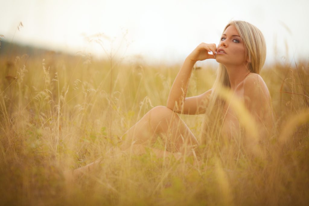 Naked blonde woman sitting in a hay field